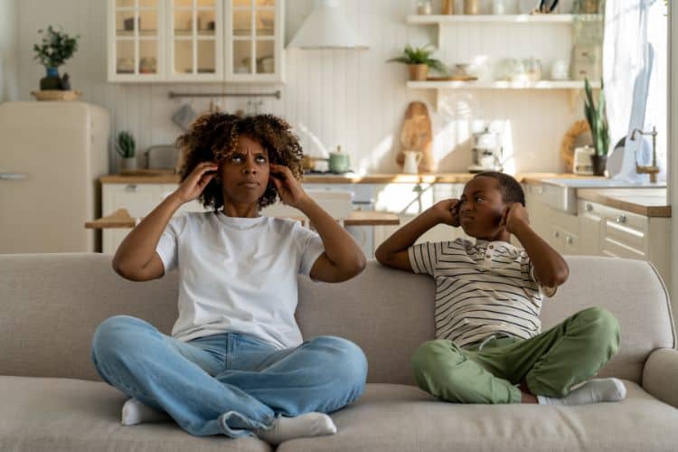 Annoyed Mother and Son Sitting on the Couch Covering Their Ears Because of a Noisy Neighbour